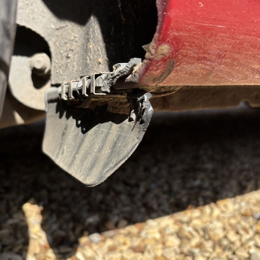 The original deflector cracked and hanging away from its mounting clips under the rear arch of a red Ford Fiesta