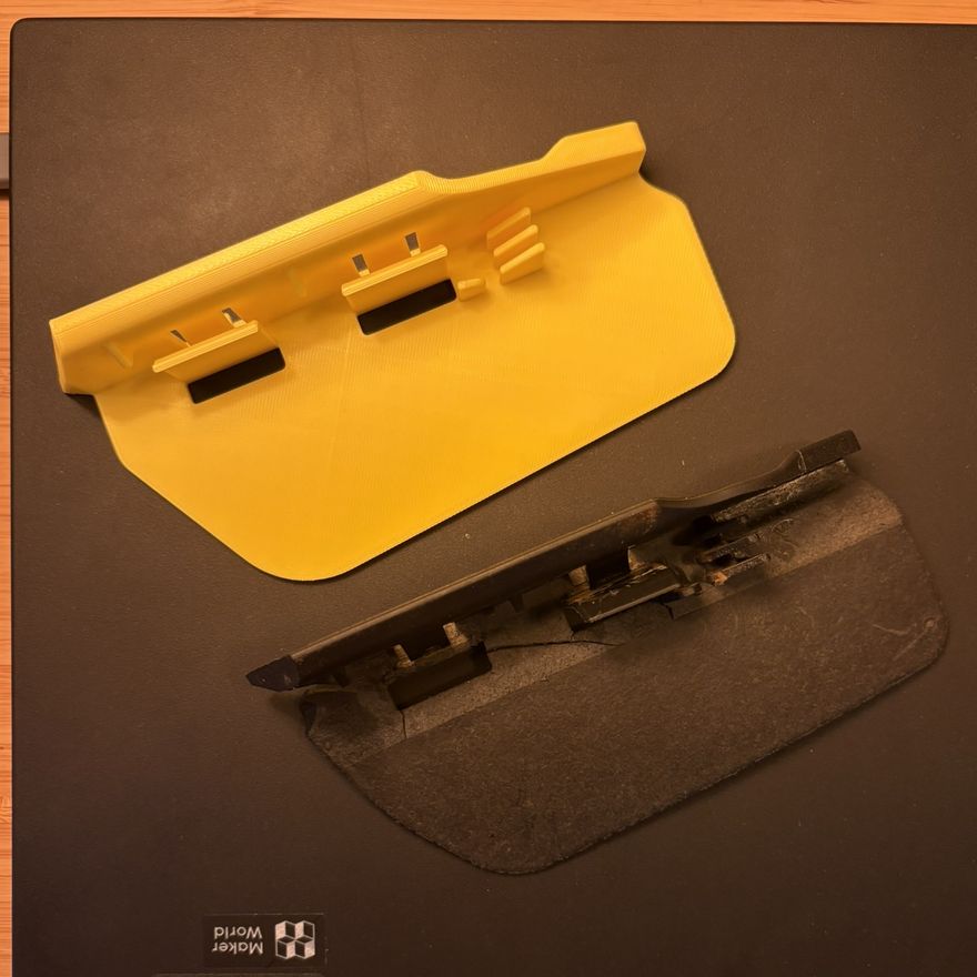 The freshly printed yellow deflector beside the worn black original on a Bambu Lab build plate