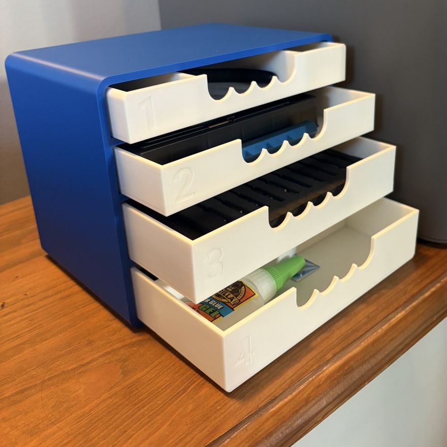 The printed blue-and-white drawer unit in use beside the printer, holding tools, filament and glue