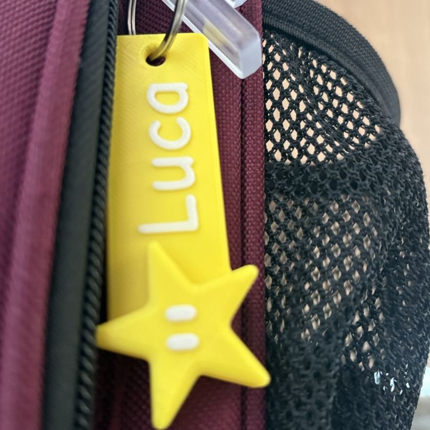 The finished yellow name tag with a star charm clipped to a school backpack zip