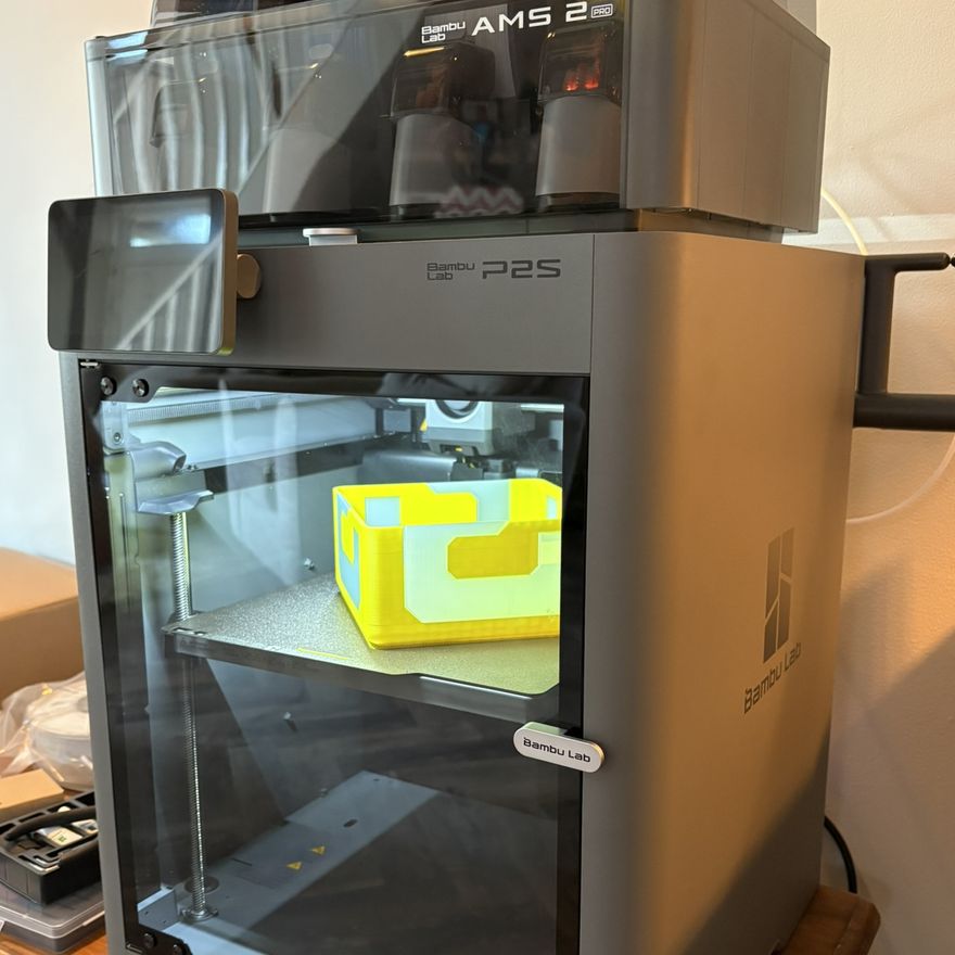 The lamp part-printed in yellow and white on a Bambu Lab P2S with the AMS 2 Pro loaded above